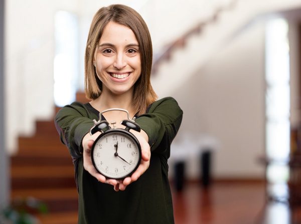 a woman smiling while holding an alarm clock