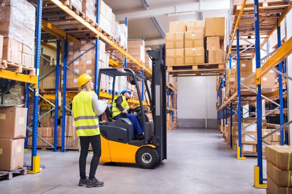 Warehouse workers stacking cardboard boxes on a pallet rack using a fork lift