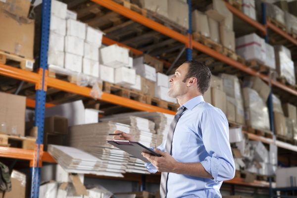 A warehouse manager checking the top shelf inventory while holding a clipboard